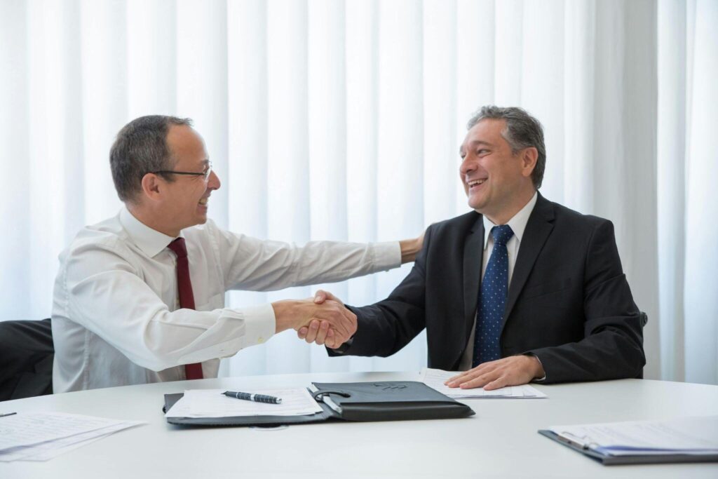 Two professionals shaking hands and smiling.