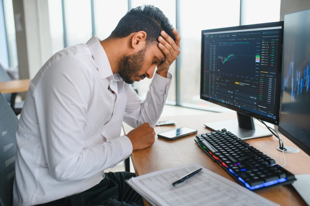 Side view of smart Indian crypto trader, investor, analyst broker, using laptop and smartphone analyzing digital cryptocurrency exchange, stock market charts, thinking of investing and funds risks.